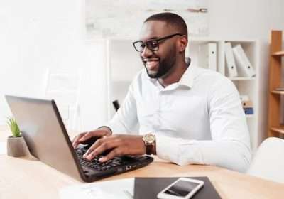 portrait-smiling-african-american-businessman-white-shirt-eyewear-sitting-working-his-laptop-office-isolated_574295-456